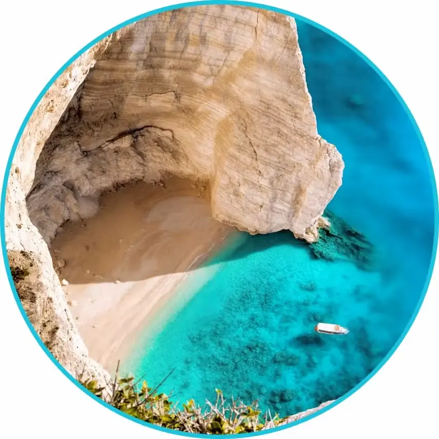 Aerial view of a secluded sandy cove beneath white limestone cliffs with crystal clear turquoise water and a small boat floating near the shore