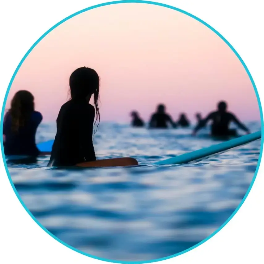 People sitting on surfboards in the ocean at sunset, representing community, calm, and an active lifestyle