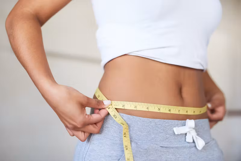 Person measuring waist with a tape measure, representing weight loss progress and body measurement