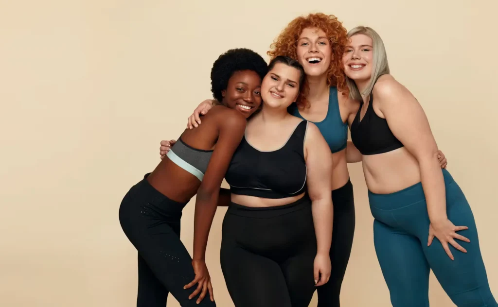Four women of diverse body types wearing activewear, smiling and standing together.